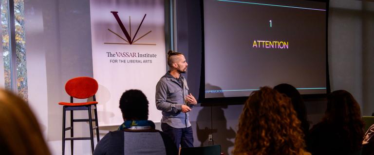 Person standing in front of a seated audience while addressing them.