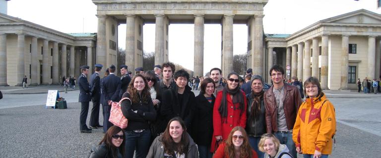 Group of students posing for a photo in front of Berlin’s Brandenburg Gate, with other visitors in the background.