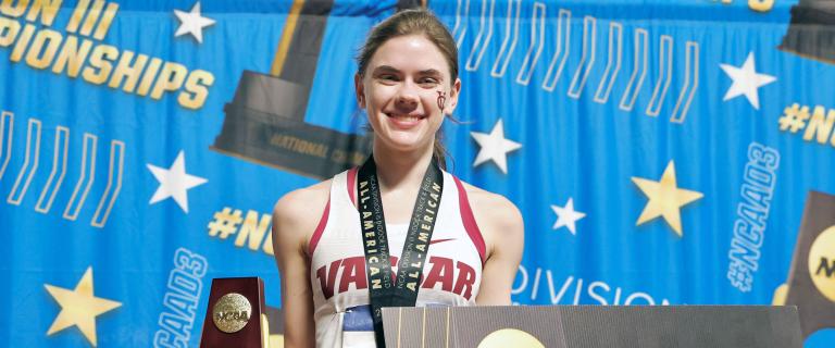 Smiling track athlete holding a trophy at an award ceremony.