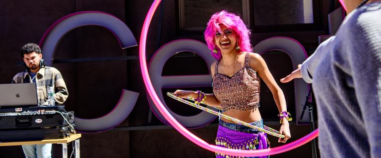 A deck on stage behind the decks while another person uses a hoola hoop.