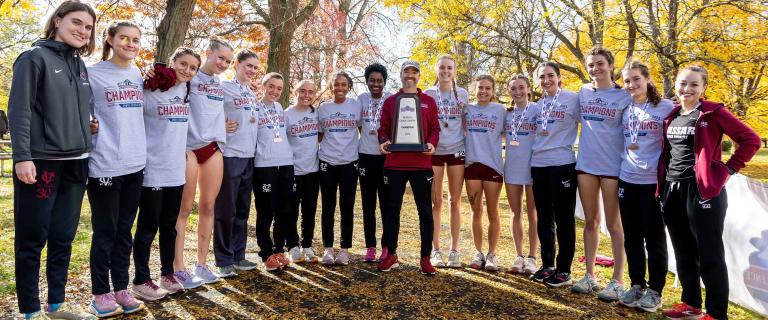 A small group of people wearing athletic gear and sweatshirts that say Champions stand in a semi-circle around a person holding a trophy.