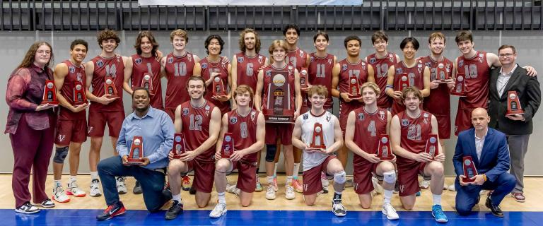 A group of people holding NCAA Volleyball Championship trophies and wearing athletic gear smile at the viewer.