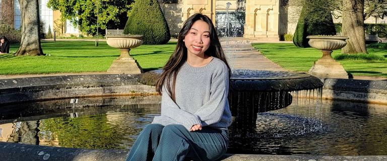 Smiling person seated in front of a fountain.