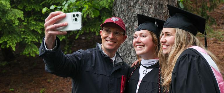 Two graduates and another person posing for a selfie.
