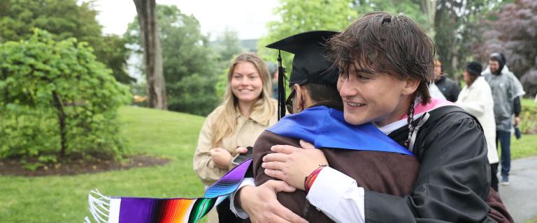 A smiling graduate hugging someone.