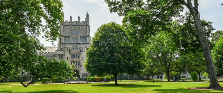 Building nestled among trees behind a large green lawn on a sunny day.