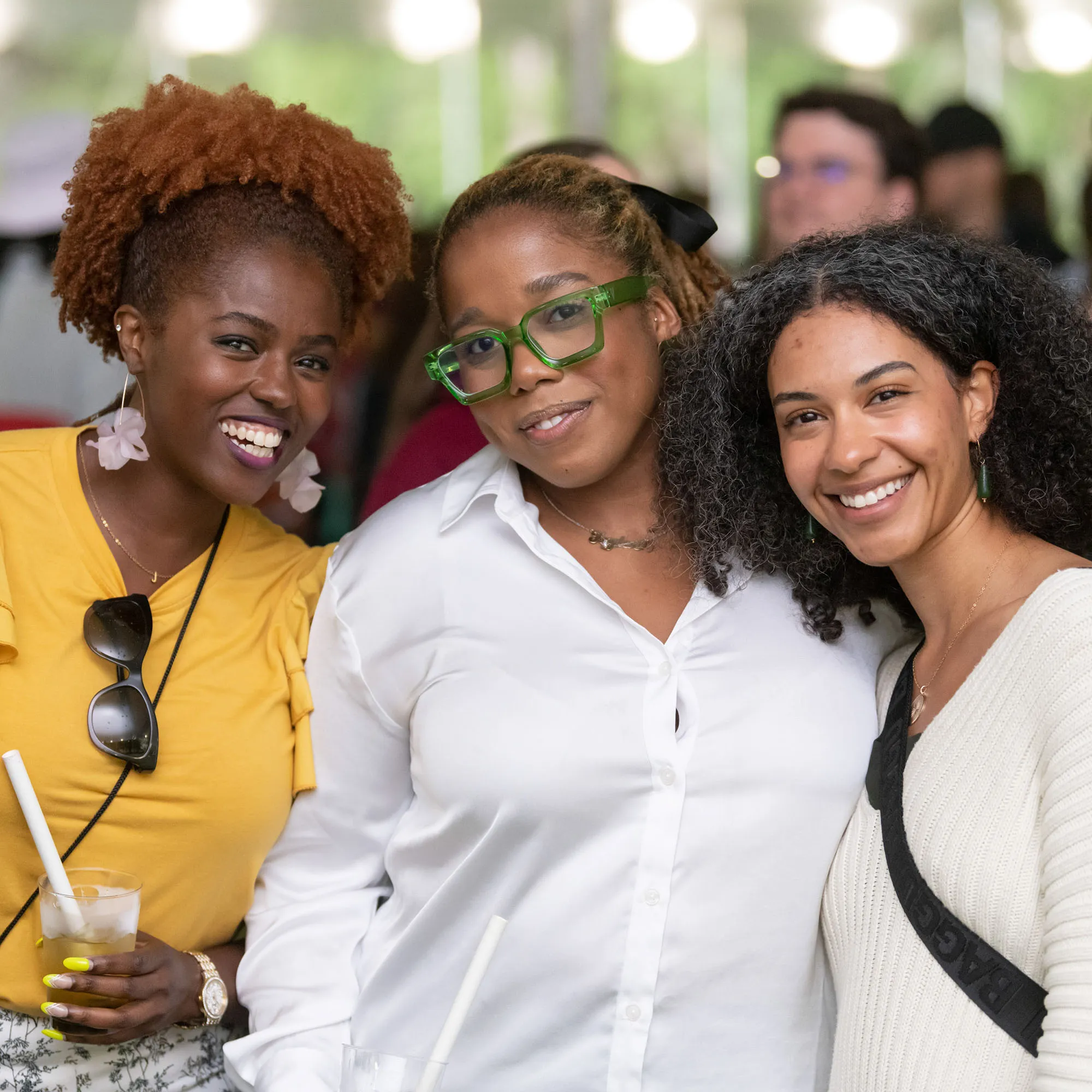 alt="A group of three people in casual attire, standing side by side, smile at the viewer."