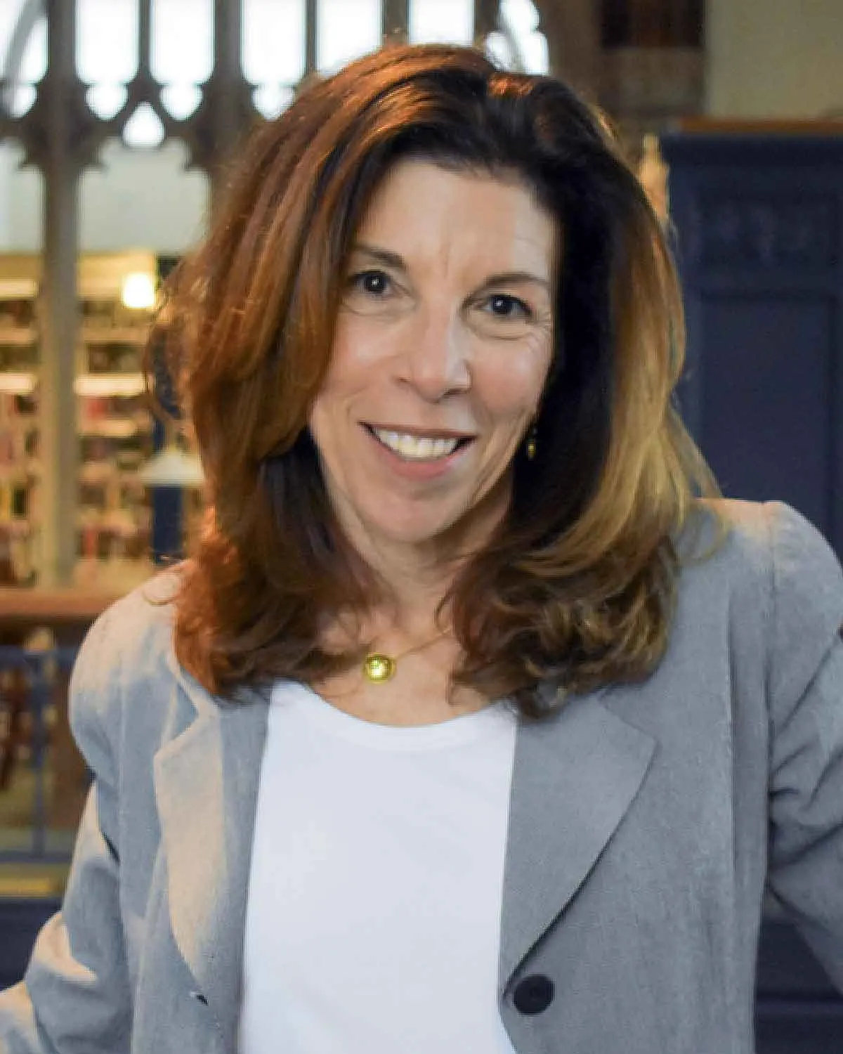 A person with long straight brown hair and a gray coat smiles at the camera