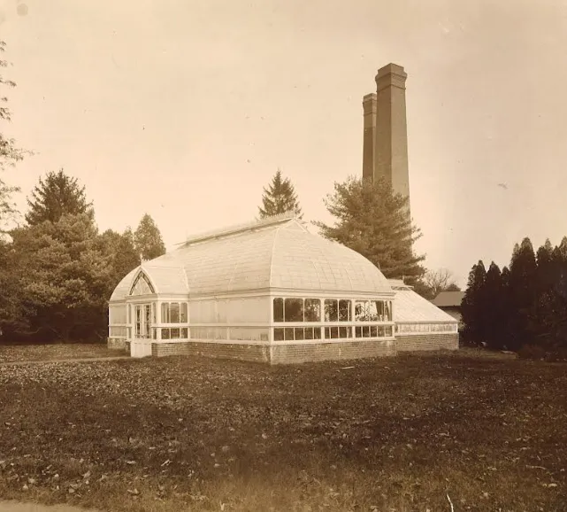 Historic photograph of the Eleanor II Conservatory with two tall chimneys rising behind it.