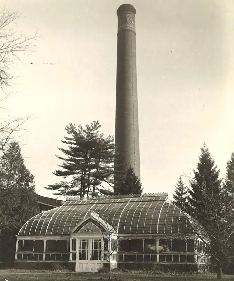 Historic photograph of the Eleanor III Conservatory with a tall brick chimney rising behind its curved glass roof.