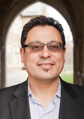 David Eduardo Tavarez wearing a light patterned shirt and black jacket in front of an archway.