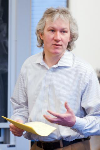 Joseph M. Tanski wearing a light striped shirt and tan pants holding a piece of paper. 