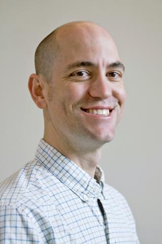 Justin C. Touchon wearing a white, square patterned shirt against a light background.