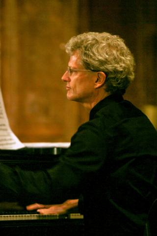 Jon Chenette wearing a black shirt sitting at a piano.