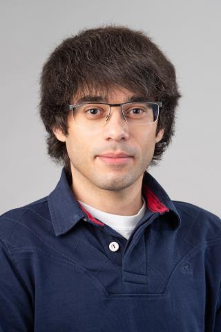 Rui Pacheco Meireles wearing a navy collared shirt against a gray background.