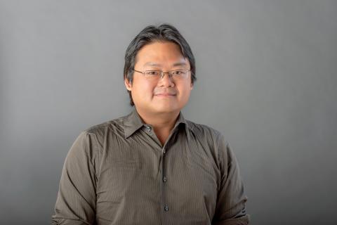 Benjamin Ho wearing a dark tan shirt against a light gray background.