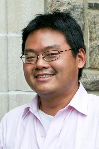 Benjamin Ho wearing a light pink collared shirt standing in front of a stone building.