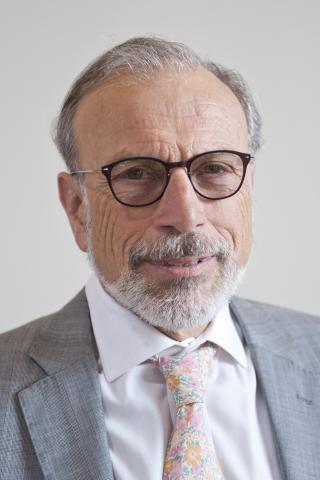 Robert DeMaria wearing a white shirt, gray jacket and floral tie against a light background.