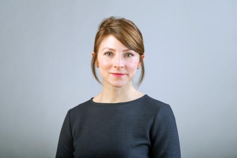 Anne Brancky wearing a black shirt against a light gray background.