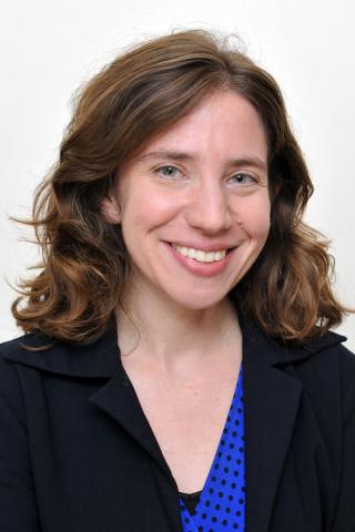 Dara N. Greenwood wearing a blue top and black jacket against a light background.