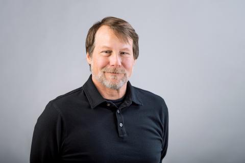 William Hoynes wearing a black collared shirt with a gray background.