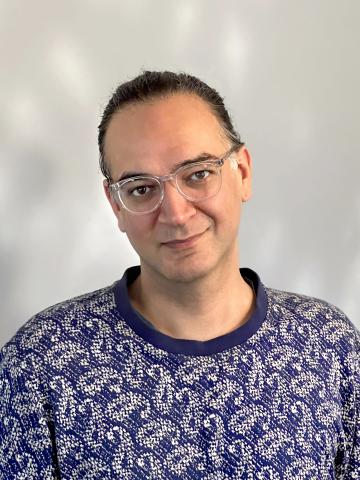 A portrait of a person with dark hair and glasses looking at the camera.