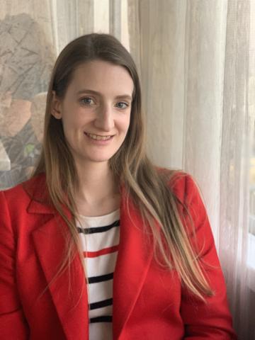 A person with long hair and a red coat smiles at the camera.