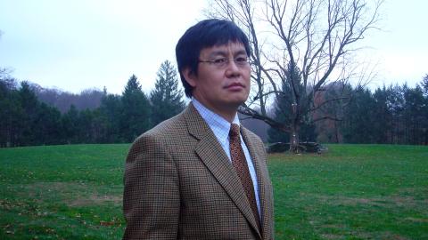 Pictured: Haoming Liu - Man with a suit and glasses standing outside with grass and trees in the background.