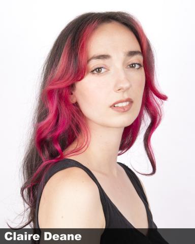 A photograph of a person with long, crimson hair wearing a black tank top and looking at the camera