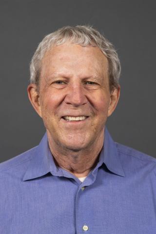 Man with grey hair and a blue button-down collared shirt smiling