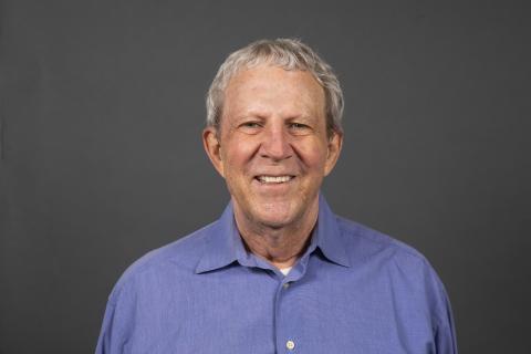 Man with grey hair and a blue button-down collared shirt smiling