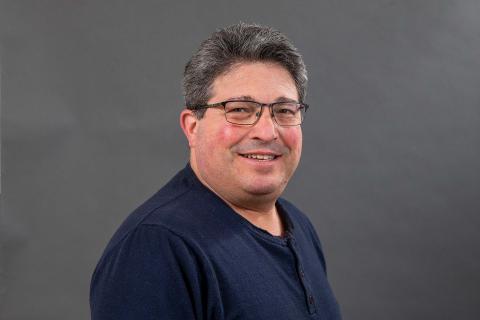 Marc Smith wearing a navy blue shirt against a gray background.