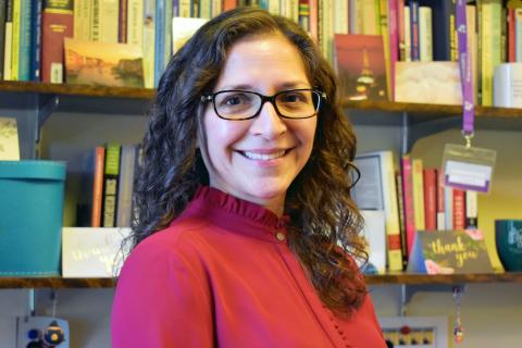 Erendira Rueda wearing a red shirt standing in front of a bookcase.