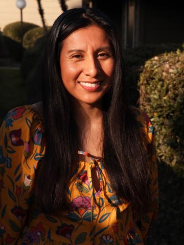 Candy Martinez headshot wearing an orange flower patterned shirt and has long dark hair.