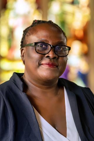 A photo of Patricia Achiro Olwoch, a person with short black hair, glasses, and a black jacket.