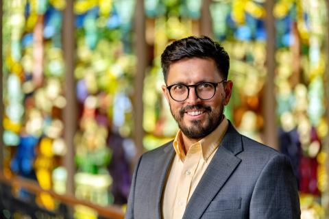 A person smiling with a colorful stained glass window in the background.
