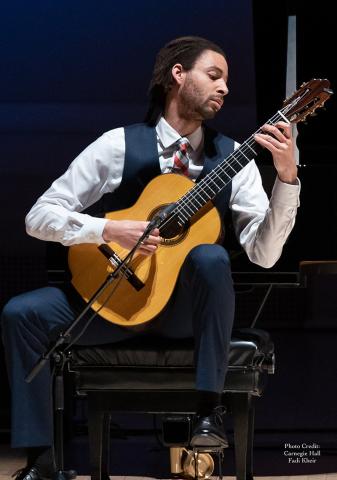 A performer playing the guitar on stage, seated.