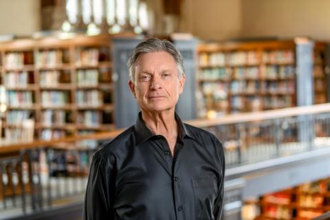 A headshot of John Meehan, a person with gray hair and a black shirt.