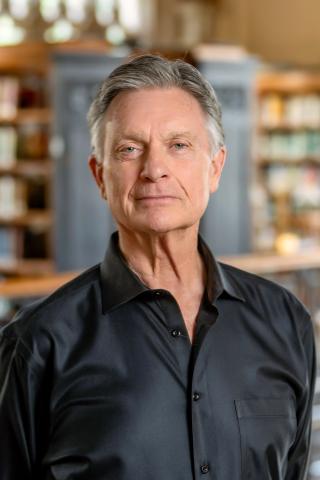A headshot of John Meehan, a person with gray hair and a black shirt.
