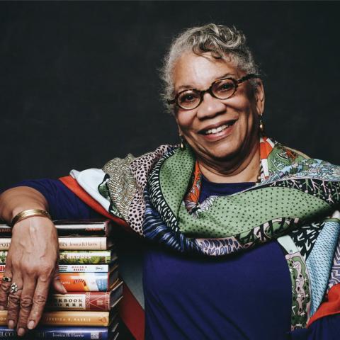 Photo of culinary historian Jessica B. Harris leaning on a stack of books.