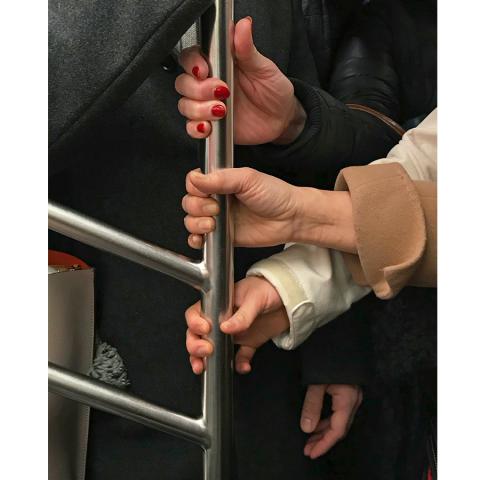 a closeup of three hands grasping a subway pole.
