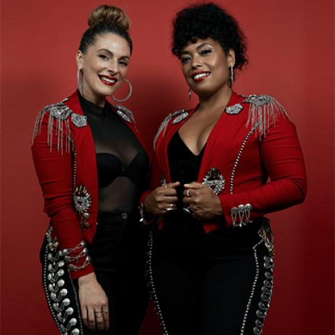Two women in red and black Mariachi outfits standing against a red background.