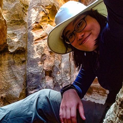 Physicist Janet Sheung perched inside a slot canyon and wearing a broad-brimmed hat.