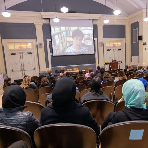 Fatemeh Sadeghi speaking via Zoom on a screen in an auditorium full of people