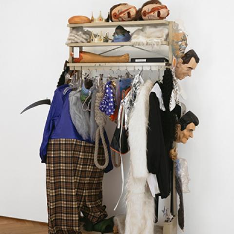 an art installation featuring a clothing rack hung with garments, masks and wigs.