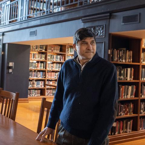Ronald Patkus standing at a table in the Vassar Library with book shelves behind him.