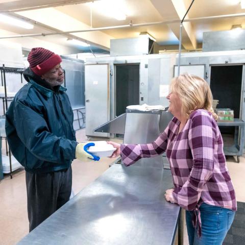 One person handing another a take-out box of food