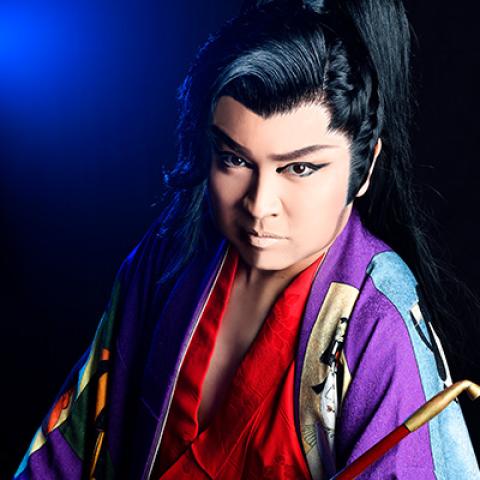 A dramatic portrait of a performer wearing long robes, an elaborate hairstyle and lots of eye makeup.