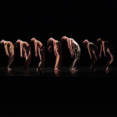 seven dancers bend backwards on a dark stage