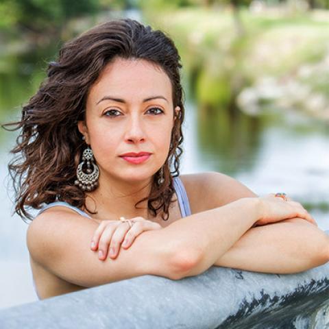 Jennine Capó Crucet leaning on a metal railing with a pond in the background.